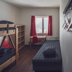 Einfaches Zimmer mit Stockbett, Zusatzbett und Kleiderablage | © Davos Klosters Mountains