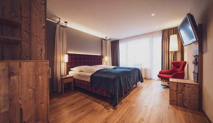 Doppelbettzimmer mit Balkon, klassischer Arveneinrichtung, Lounchsessel, Kommode und Holzboden | © Davos Klosters Mountains 