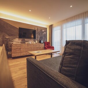 Grosses Zimmer mit Holzboden, Sofa, Holzkommode und Fernseher | © Davos Klosters Mountains 