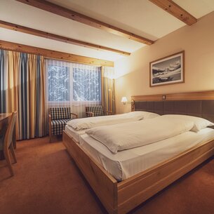 Doppelbettzimmer mit grossen Fenstern, Vorhängen und Teppichboden  | © Davos Klosters Mountains 