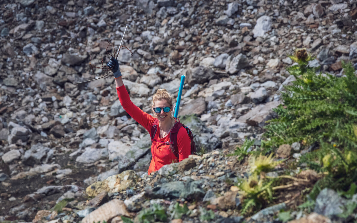 Eine rot gekleidete Helferin der Aufräumaktion auf Parsenn hält ihr gefundenen Abfall in die Luft.  | © Davos Klosters Mountains