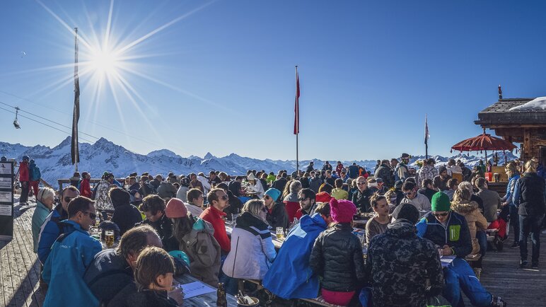 Skifahrer wie auch Fussgänger geniessen ihr Mittagessen auf der Terrasse des Chalet Güggel bei Sonnenschein. | © Davos Klosters Mountains