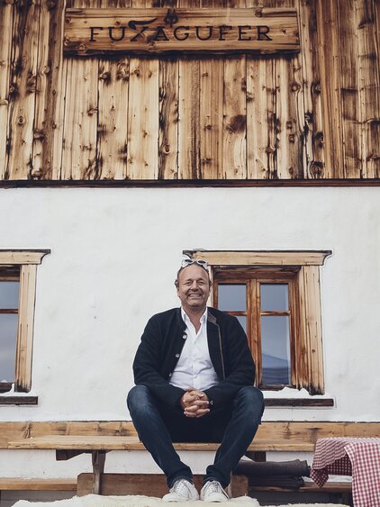 Der Pächter, Dominik Rüedi, auch Niggi genannt sitzend auf einem Tisch vor dem Restaurant Fuxägufer. | © Davos Klosters Mountains