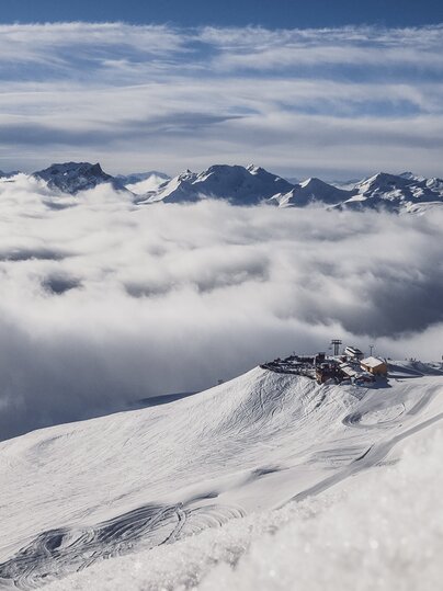 Aufnahme aus der Ferne mit Sicht auf die Jatzhütte Davos welche über den Wolken ersichtlich ist. | © Davos Klosters Mountain