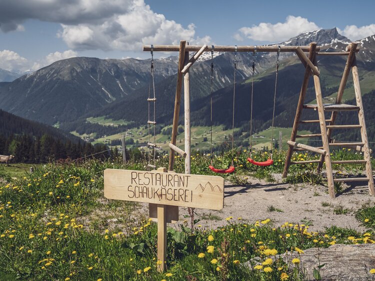 Ein kleiner Spielplatz mit zwei Schaukeln und einem Kletterturm steht neben dem Restaurant Schaukäserei. | © Davos Klosters Mountains