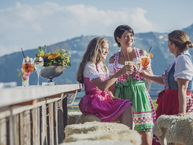 Drei Frauen genießen in ihrer Tracht einen Apero auf der Sonnenterrasse der Madrisa-Alp.  | © Davos Klosters Mountains
