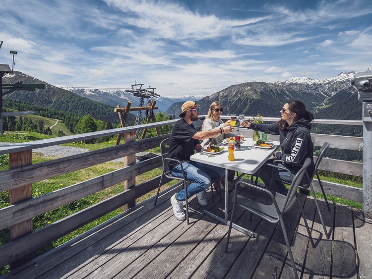 Drei Freunde sitzen auf der Sonnenterrasse des Jatzmeders und freuen sich auf ihr Essen.  | © Davos Klosters Mountains
