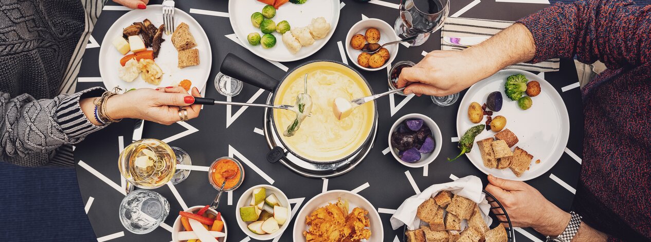 Zwei Gäste geniessen ihr Fondue mit vielen Beilagen im Restaurant Piz Piz Davos. | © Davos Klosters Mountains
