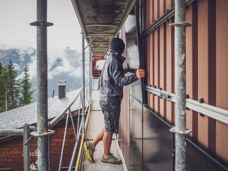 Ein Arbeiter von Solpic hängt das Solarpanel an die montierte Unterkonstruktion auf der Fassade auf Jschalp. | © Davos Klosters Mountains