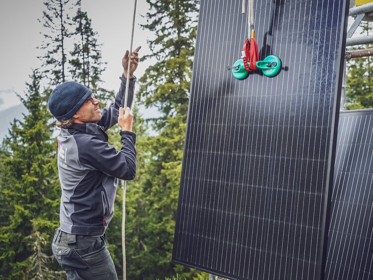 Ein Arbeiter zieht ein Solarpanel mit einem Seilzug auf das Gerüst.  | © Davos Klosters Mountains