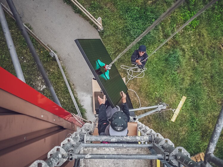 Blick aus der Vogelperspektive, wie ein Arbeiter das Solarpanel auf das Gerüst transportiert.   | © Davos Klosters Mountains