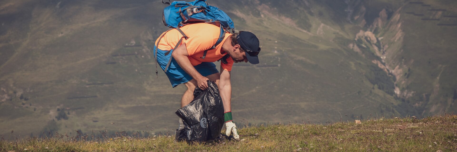 Ein Teilnehmer des Umweltcamps liest Abfall vom Boden auf und sammelt diesen in seinem Abfallsack.  | © Davos Klosters Mountains