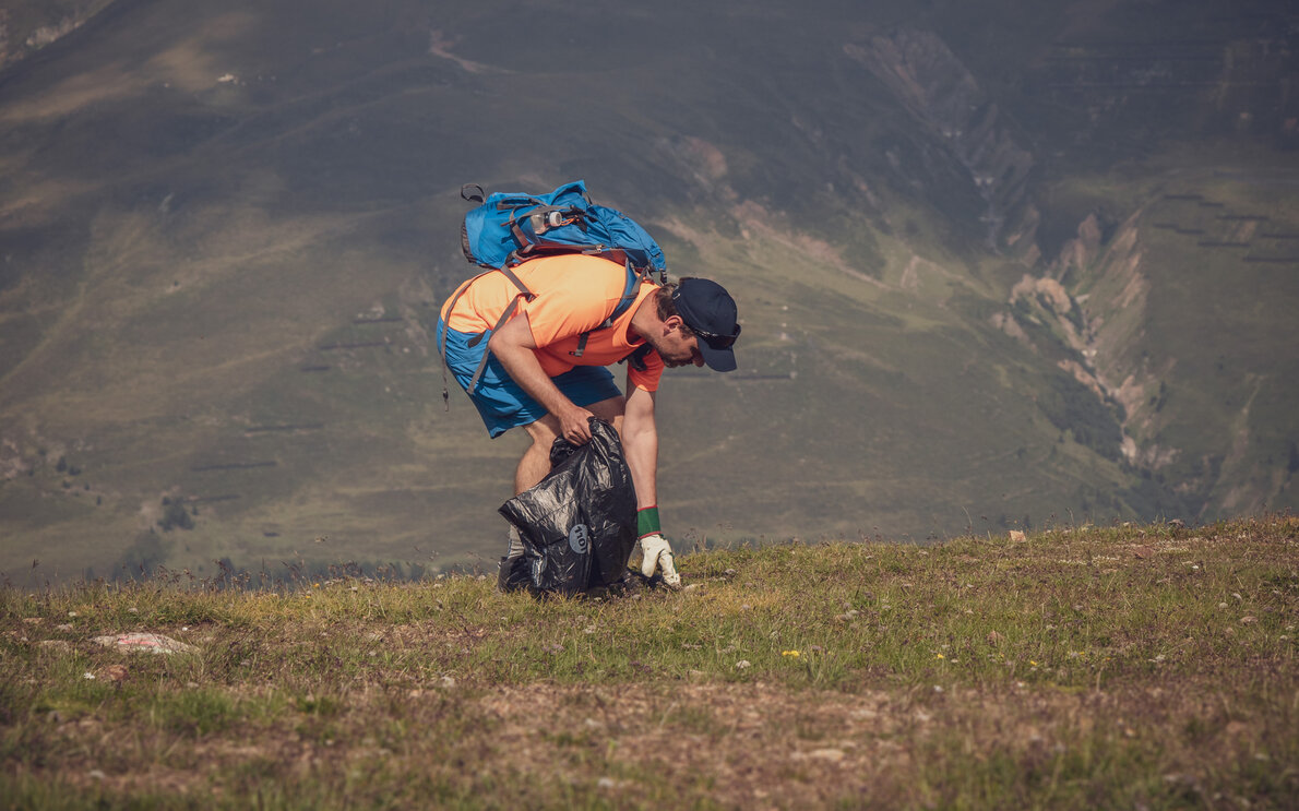 Ein Teilnehmer des Umweltcamps liest Abfall vom Boden auf und sammelt diesen in seinem Abfallsack.  | © Davos Klosters Mountains