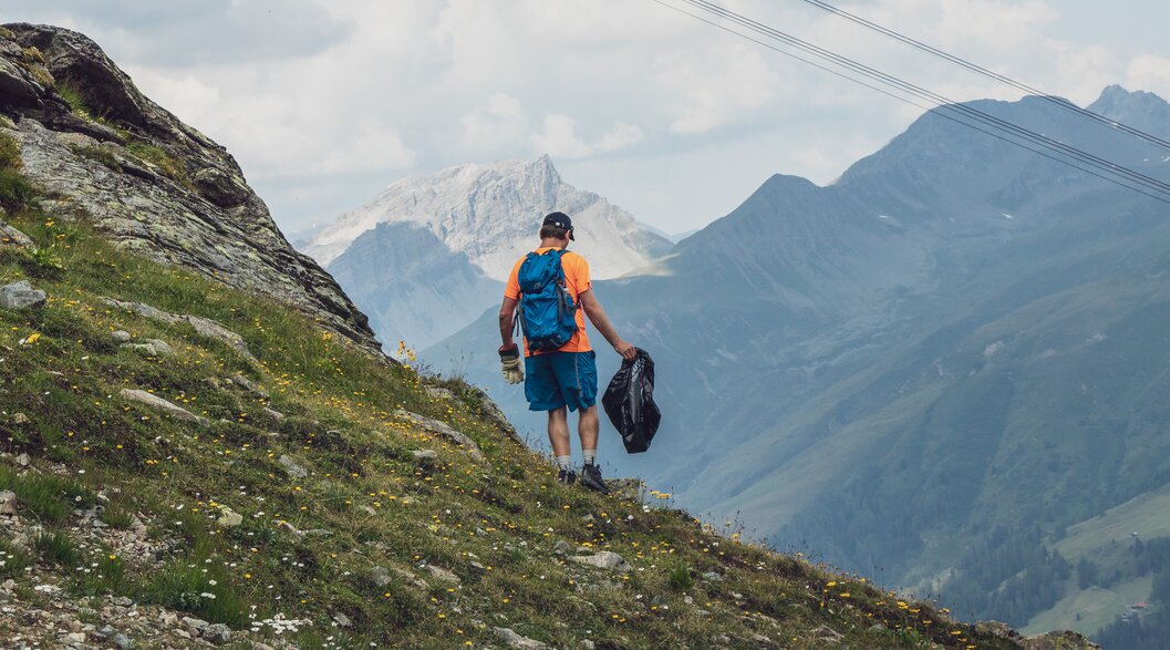 Ein Helfer sammelt Abfall auf dem Berg ein, er ist mit Handschuhen und Müllsack ausgerüstet. | © Davos Klosters Mountains