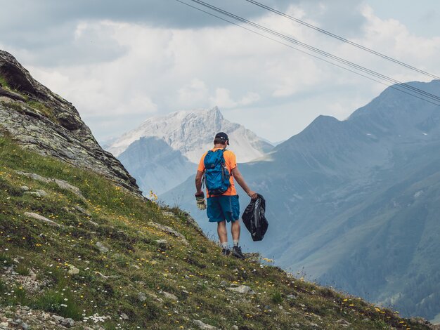 Ein Helfer sammelt Abfall auf dem Berg ein, er ist mit Handschuhen und Müllsack ausgerüstet. | © Davos Klosters Mountains