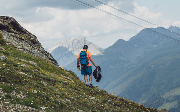 A helper collects waste on the mountain, his equipment are gloves and a garbage bag. | © Davos Klosters Mountains
