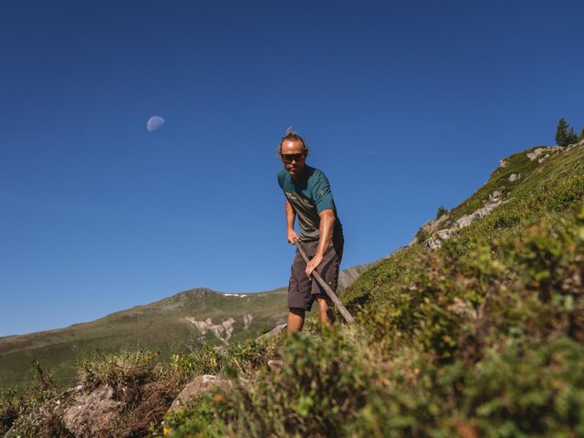 Ein Mitarbeiter der Trail Crew bessert den Weg mit einer Schaufel aus, im Hintergrund der Mond.  | © Christoph Koch