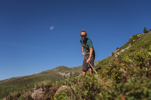 Ein Mitarbeiter der Trail Crew bessert den Weg mit einer Schaufel aus, im Hintergrund der Mond.  | © Christoph Koch