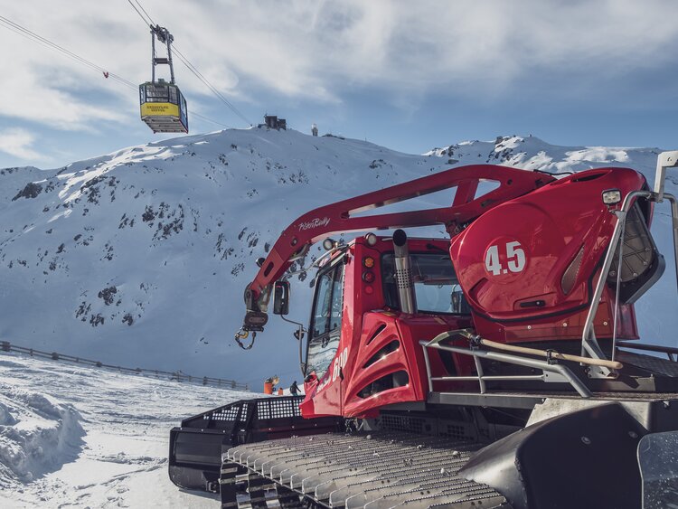 Der Pistenbully steht für die Abfahrt bereit. im Hintergrund schwebt die Gipfelbahn vorbei.  | © Davos Klosters Mountains