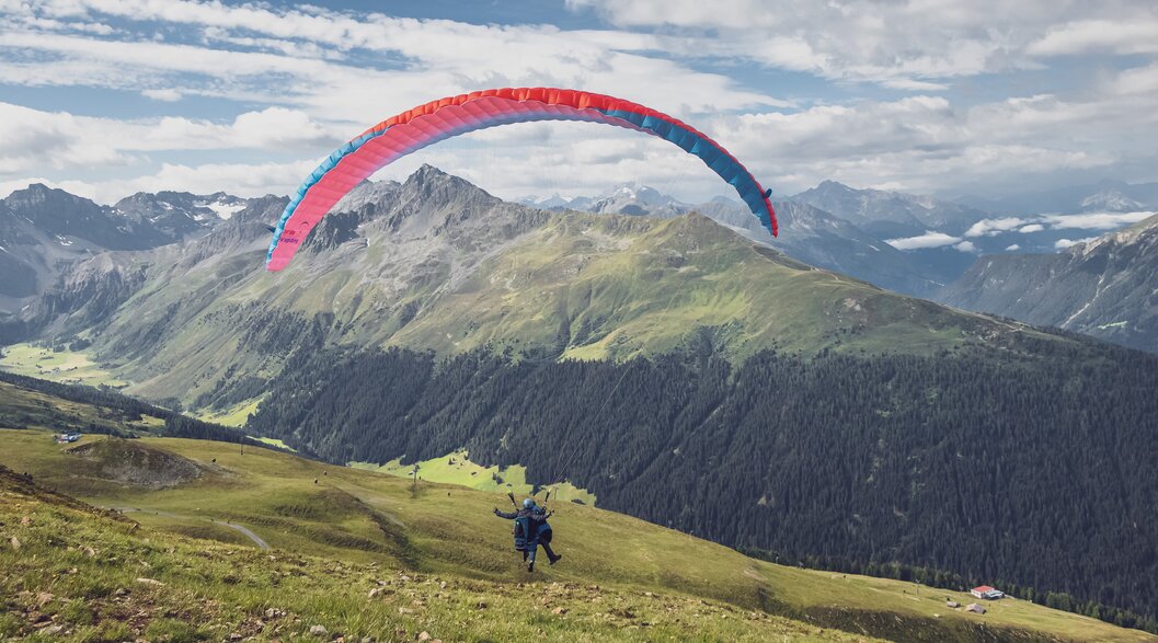 Der Gleitschirm hebt ab und die beiden Passagiere fliegen bei einem Tandemflug hinunter nach Davos.  | © Davos Klosters Mountains