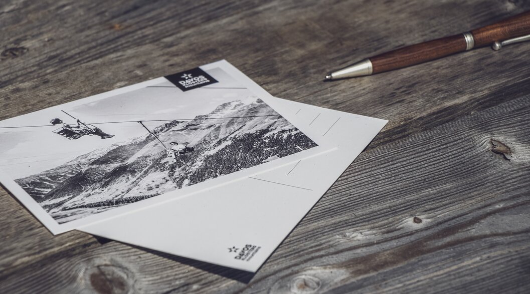 Postkarten | © Davos Klosters Mountains Zwei Retro Postkarten der Davos Klosters Mountains liegen auf einem Tisch zusammen mit einem Stift. | © Davos Klosters Mountains