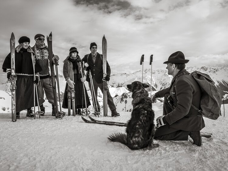 Eine Gruppe Skifahrer nostalgisch gekleidet hört dem Rettungschef mit Hund zu.  | © Davos Klosters Mountains