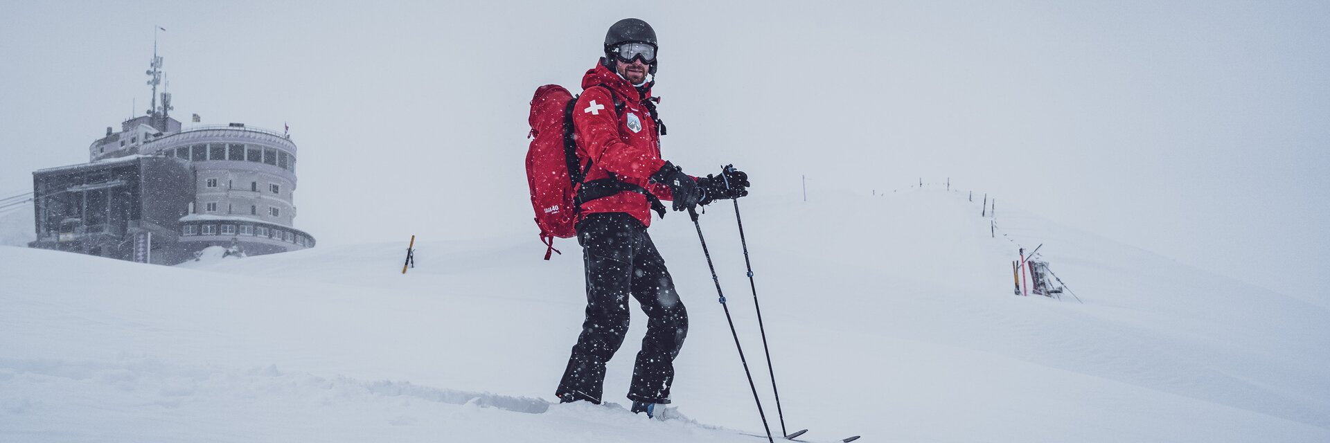 Patrouilleur im Einsatz | © Davos Klosters Mountains Michi vom Rettungsdienst Jakobshorn ist mit den Skiern im Einsatz, hinter ihm die Bergstation Jakobshorn. | © Davos Klosters Mountains