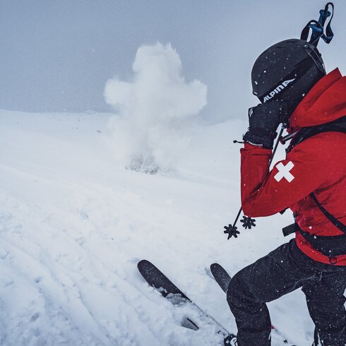 Der Patrouilleur vom Jakobshorn hält sich die Ohren zu und der Sprengkörper explodiert im Schnee. | © Davos Klosters Mountains