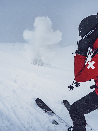 Der Patrouilleur vom Jakobshorn hält sich die Ohren zu und der Sprengkörper explodiert im Schnee. | © Davos Klosters Mountains