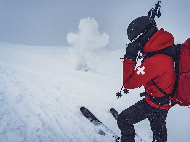 Explosion bei der Lawinensprengung | © Davos Klosters Mountains Der Patrouilleur vom Jakobshorn hält sich die Ohren zu und der Sprengkörper explodiert im Schnee. | © Davos Klosters Mountains