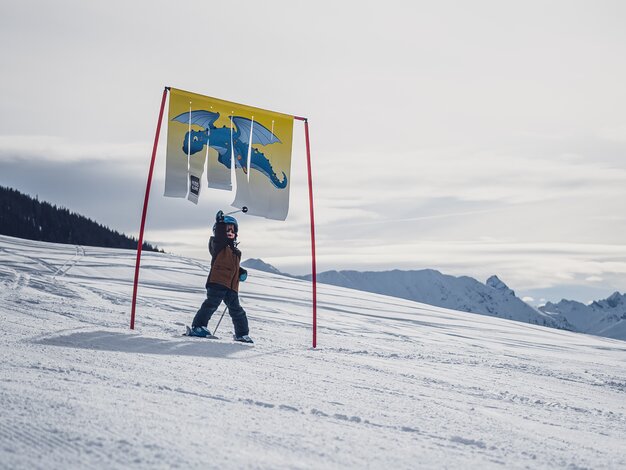 Ein Kind fährt durch ein Tor der Kidsslope beim Bolgen und berührt mit dem rechten Arm die flatternde Plane.  | © Davos Klosters Mountains