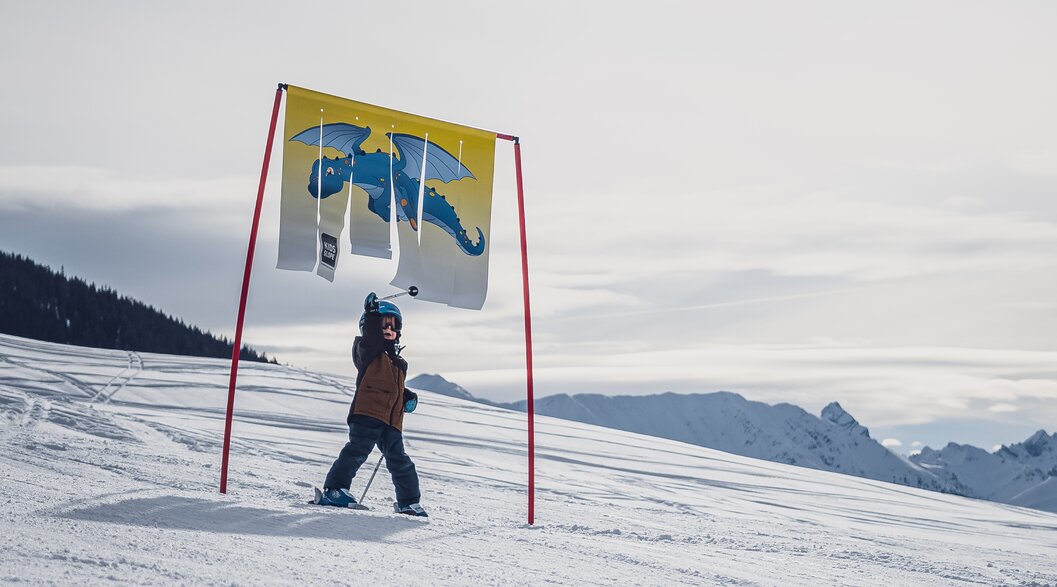 Kleinkind unter Torstange mit Drachenwimpel | © Davos Klosters Mountains Toddler under gate pole with dragon pennant | © Davos Klosters Mountains