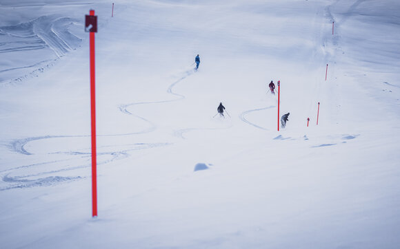 Skifahrer ziehen ihre ersten Kurven auf der mit Pulverschnee bedeckten Abfahrt. | © Davos Klosters Mountains