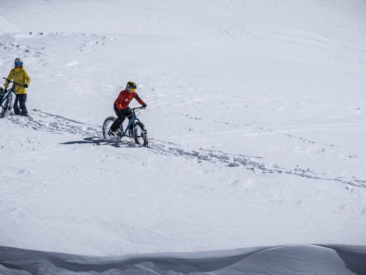 Mann und Frau fahren mit Ihren Fatbikes im Tiefschnee den Berg hinunter. | © Davos Klosters Mountains