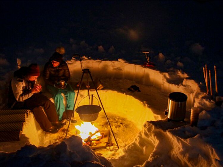 Um das Feuer sitzend geniessen die Gäste die Wärme und den heissen Tee.  | © Davos Klosters Mountains