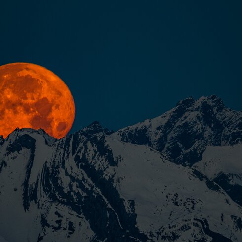 A red full moon rises behind the snowy mountain ridge. | © Davos Klosters Mountains