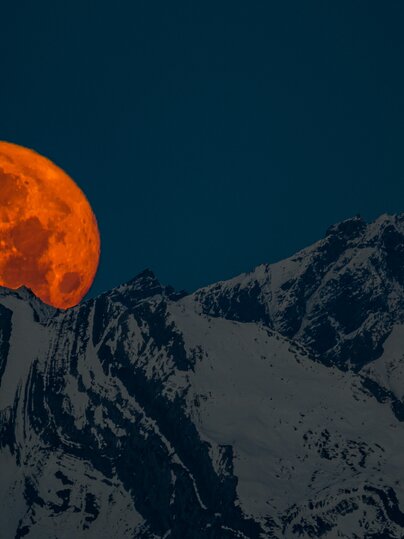 Ein roter Vollmond erhebt sich hinter dem verschneiten Bergkamm. | © Davos Klosters Mountains
