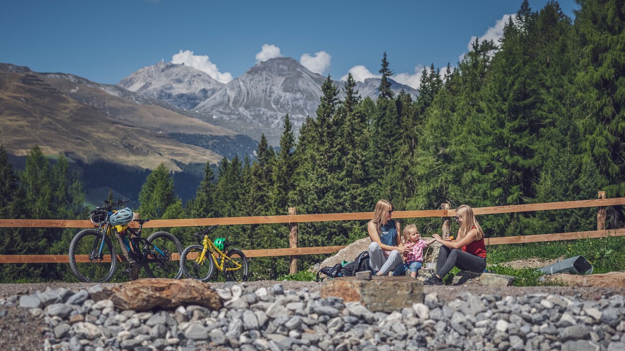 Zwei Frauen und ein Mädchen sitzen am Ufer eines Bergsees, daneben steht ein grosses und ein kleines Bike. | © Davos Klosters Mountains