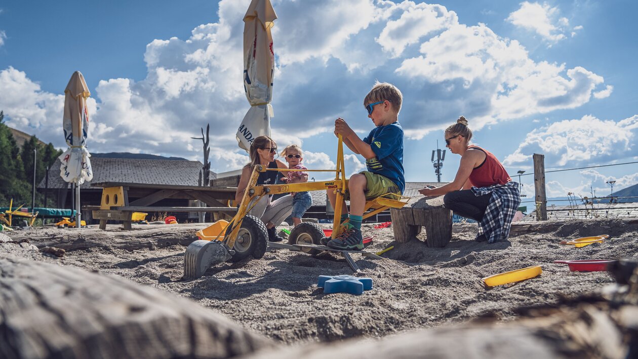 2 Kinder und 2 Erwachsene Personen sind im Sandkasten und spielen miteinander.  | © Davos Klosters Mountains
