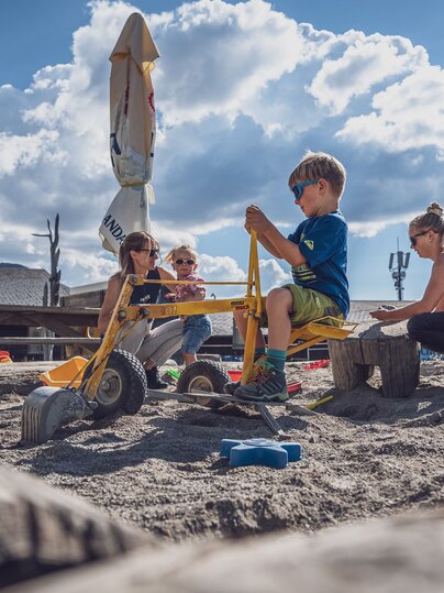 2 Kinder und 2 Erwachsene Personen sind im Sandkasten und spielen miteinander.  | © Davos Klosters Mountains