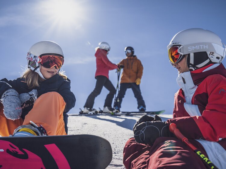 Zwei Mädchen mit ihren Eltern im Hintergrund machen eine Pause auf der Piste. | © Davos Klosters Mountains