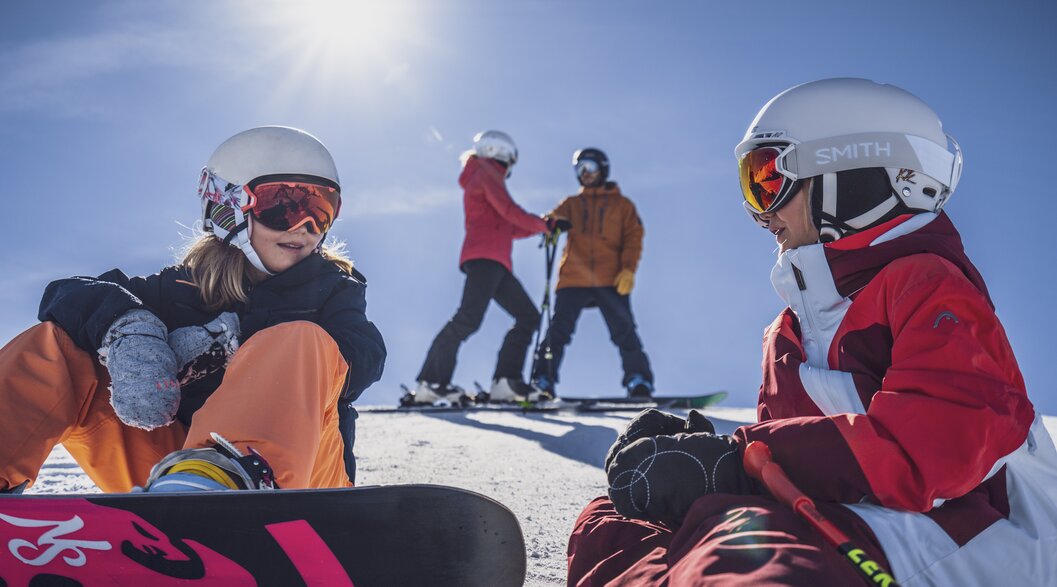 Family day at the Rinerhorn | © Davos Klosters Mountains Two girls with their parents in the background take a break on the slopes. | © Davos Klosters Mountains