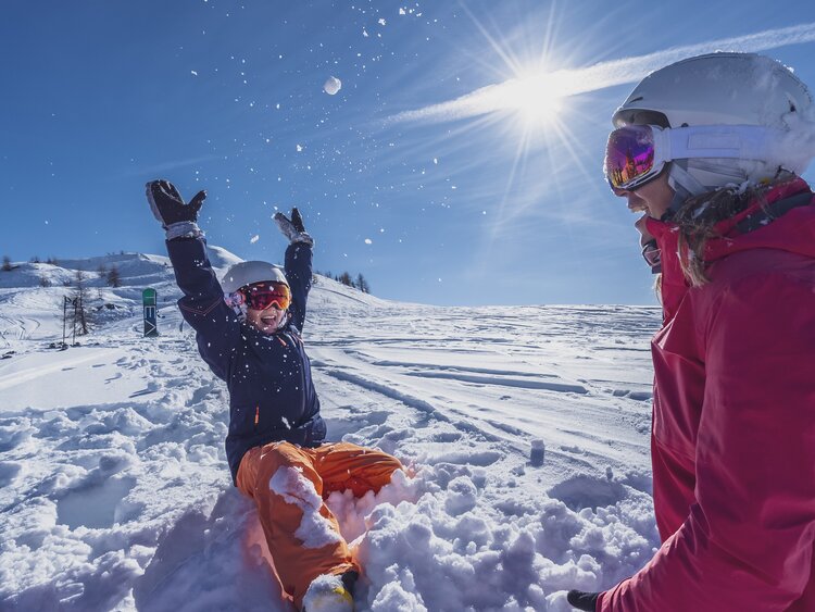 Mutter und Tochter spielen im Tiefschnee bei Sonnenschein. | © Davos Klosters Mountains