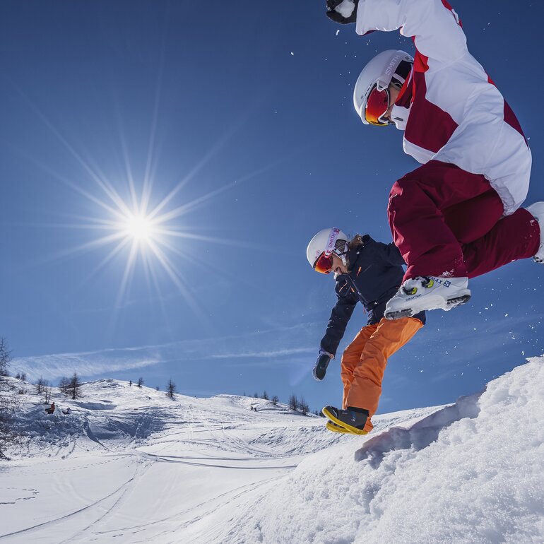 Kinder springen in den Schnee während dem die Sonne strahlt. | © Davos Klosters Mountains