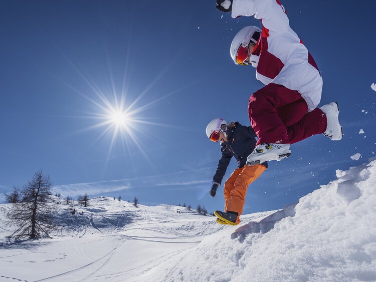 Kinder springen in den Schnee während dem die Sonne strahlt. | © Davos Klosters Mountains