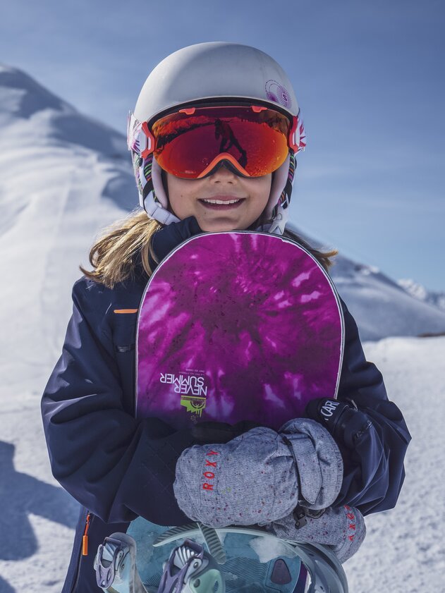 Snowboarder Mädchen | © Davos Klosters Mountains Junges Mädchen mit Never Summer Snowboard in der Hand und ihrer Famile im Hintergrund. | © Davos Klosters Mountains