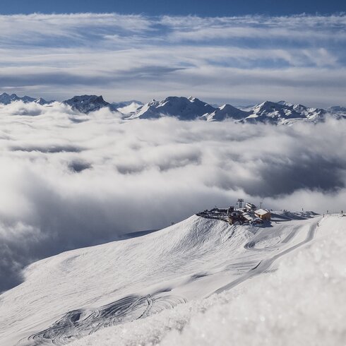 Shot from far away with a view of the Jatzhütte Davos which can be seen above the clouds. | © Davos Klosters Mountain