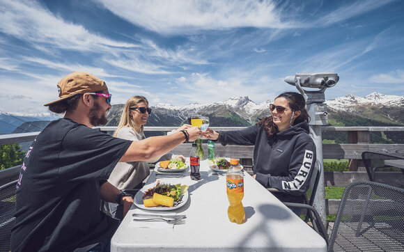 Drei Freunde stossen an und freuen sich auf Ihr Mittagessen auf der Sonnenterrasse Jatzmeder. | © Davos Klosters Mountains