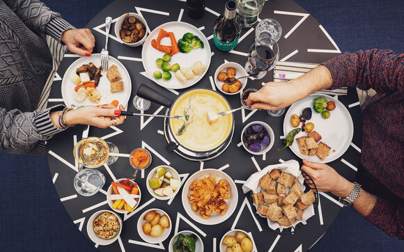 Two guests enjoy their fondue with many side dishes in the Piz Piz Davos restaurant. | © Davos Klosters Mountains