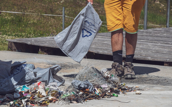 A man with yellow pants empties his full garbage bag on the ground where the collection is.  | © Davos Klosters Mountains